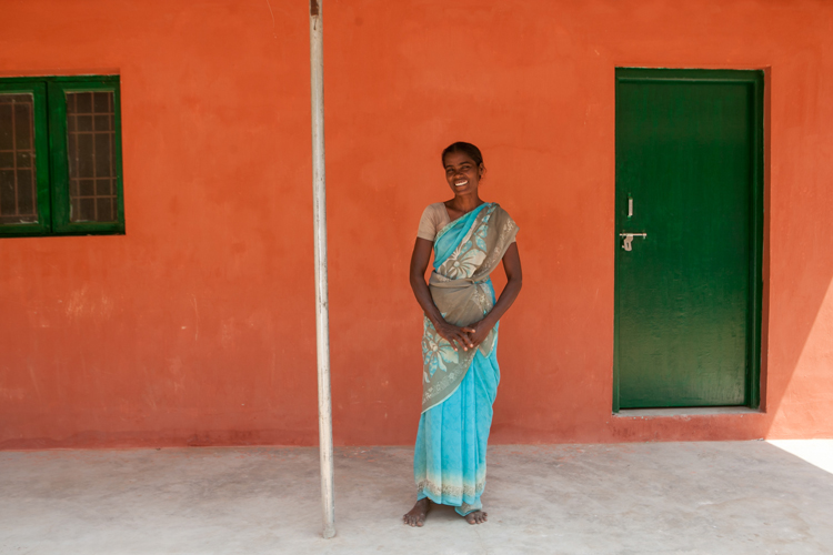 Manjula stands joyfully on her front step, behind her is a new green door