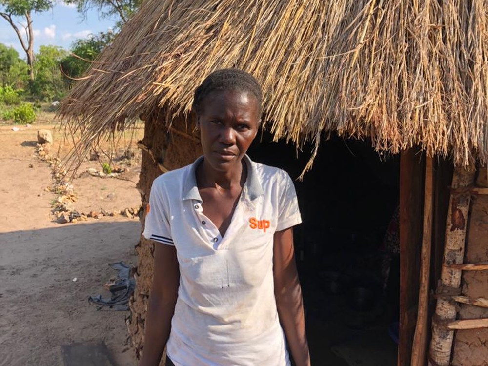Asililo standing in front of her old thatched hut in rural Zambia