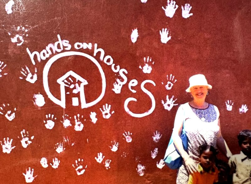 Children's white handprints on a terracotta wall with the Hands on Houses logo
